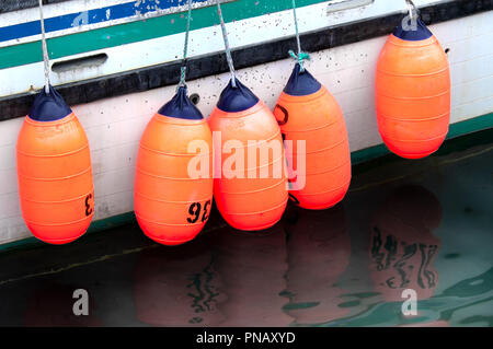 Colorful orange and blue buoys hang over the side of an old fishing boat in the harbor in Seldovia, Alaska. Stock Photo