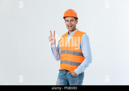 Young workman with helmet happy and counting two with fingers on green background Stock Photo