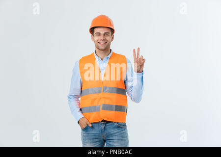 Young workman with helmet happy and counting two with fingers on green background Stock Photo