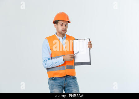 Frustrated young engineer with hardhat and reflective vest checking on mistake in document over gray background Stock Photo