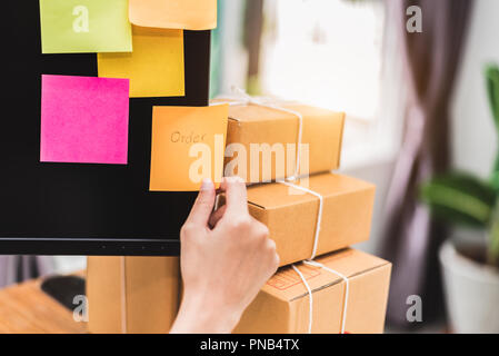 Close up hand putting sticker memo note on computer display screen as business entrepreneur owner shop in delivery service home office. Drop shipping  Stock Photo