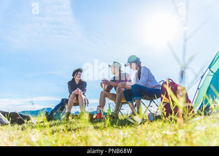 Group of travelers camping and doing picnic in meadow field foreground. Mountain and lake background. People and lifestyles concept. Outdoors activity Stock Photo