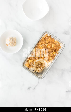 Homemade Toffee apple ice cream with vanilla ice cream, apples, toffee sauce and cinnamon crumbles in metal container and bowl. Stock Photo