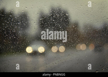 Cars with headlights on viewed through a raindrop-covered windshield. Stock Photo