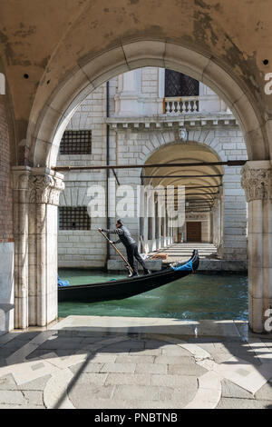 Venice, Italy - March 21, 2018: Venetian gondolier riding gondola through the side narrow canal in Venice. Stock Photo