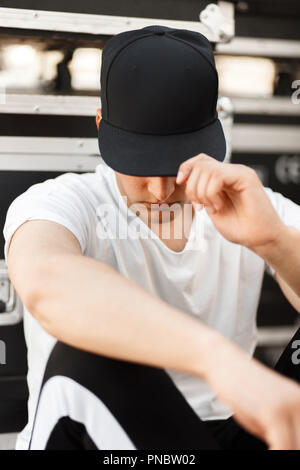 Fashionable young man with a black cap covers the face and sits on the street Stock Photo