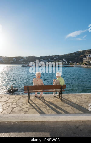 Batsi, Greece - May 31, 2018: Unidentified senior ladies talks at seafront bench in picturesque village of Batsi on Andros island, Cyclades, Greece Stock Photo