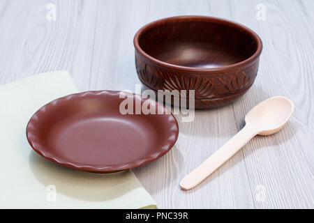 Empty brown clay plate and bowl with wooden spoon and napkin on gray desk Stock Photo