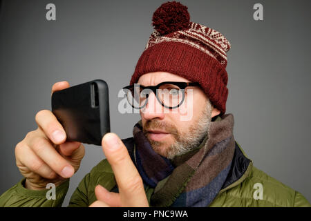 Funny european adult in warm hat and scarf man using smartphone application. Studio shoot Stock Photo