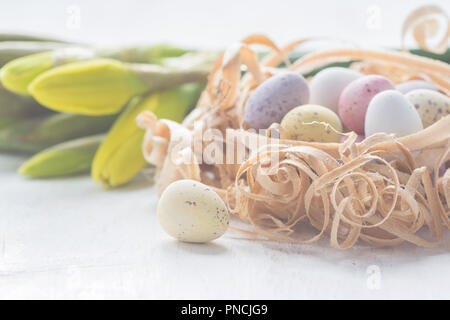 Coloured chocolate eggs in nest made from wood shavings close up, selective focus. Warm pastel toned macro photo Stock Photo