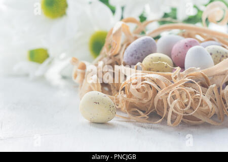 Coloured chocolate eggs in nest made from wood shavings close up, selective focus. Warm pastel toned macro photo Stock Photo