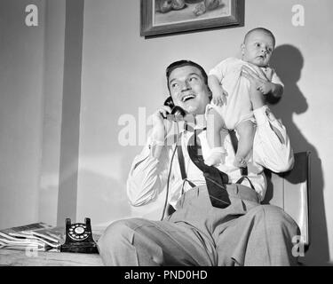 1940s 1950s MAN FATHER TALKING ON TELEPHONE HOLDING BABY BOY UP WITH ONE HAND - b809 DEB001 HARS INFANT SONS JOY LIFESTYLE HOME LIFE COMMUNICATING COPY SPACE FULL-LENGTH HALF-LENGTH PERSONS MALES FATHERS B&W DADS LOW ANGLE PRIDE UP NECKTIE PHONES SUSPENDERS CONNECTION TELEPHONES SUPPORT DEB001 BABY BOY COOPERATION JUVENILES MID-ADULT MID-ADULT MAN BLACK AND WHITE CAUCASIAN ETHNICITY OLD FASHIONED Stock Photo