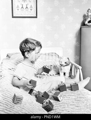 1930S 1940S YOUNG BOY SITTING IN BED PLAYING WITH TOY BLOCKS AND TOY CAT - j1149 HAR001 HARS GROWTH JUVENILES BLACK AND WHITE CAUCASIAN ETHNICITY HAR001 OLD FASHIONED Stock Photo