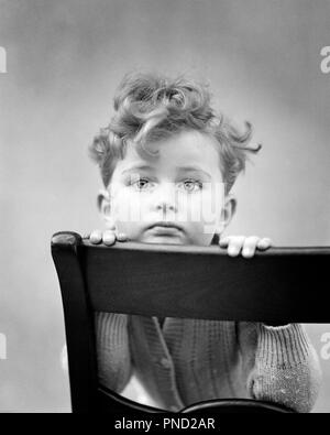 1940s DIFFIDENT CURLY HAIR BOY RESTING CHIN ON BACK OF CHAIR LOOKING AT CAMERA - j9147 HAR001 HARS SADNESS WIDE EYE CONTACT ANXIETY STARING HEAD AND SHOULDERS ANXIOUS CURLY FIXED OF ON FEELING APPREHENSION CONNECTION CONCEPTUAL GLUM WITHDRAWN SHYNESS VACANT DIFFIDENT EMOTION EMOTIONAL EMOTIONS GROWTH JUVENILES MISERABLE BLACK AND WHITE CAUCASIAN ETHNICITY HAR001 OLD FASHIONED Stock Photo