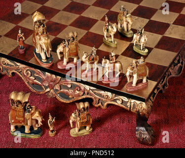 1950s CHESS SET IN STYLE OF INDIA ELEPHANTS AND MAHARAJA HUNTING PARTY ON RAISED ORNATE CHESSBOARD  - ks38472 FRT001 HARS ORNATE RECREATION IN OF ON CARVED OCCUPATIONS CHESSBOARD CONCEPTUAL STILL LIFE IMAGINATION STYLISH SYMBOLIC CAMELS HUNTERS MAHARAJA MAMMAL POLYCHROME PRECISION WILDLIFE GILDED OLD FASHIONED REPRESENTATION Stock Photo