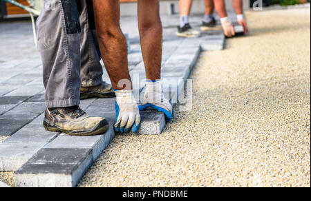 Laying gray concrete paving slabs in house courtyard driveway patio. Professional workers bricklayers are installing new tiles or slabs for driveway,  Stock Photo
