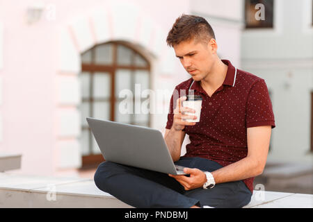 Young handsome businessman freelancer working on laptop and drinking coffee in the city Stock Photo