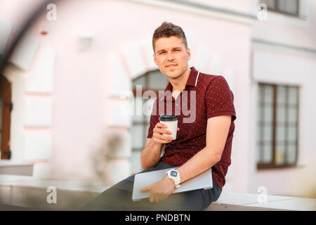 Handsome young man with laptop drinking coffee and traveling in the city Stock Photo