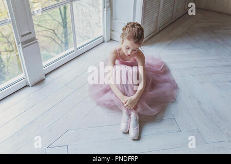 Young classical ballet dancer girl in dance class. Beautiful graceful ballerina practice ballet positions in pink tutu skirt in white light hall Stock Photo