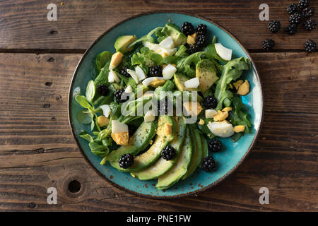 Avocado salad with eggs, lamb's lettuce, blackberry and arugula on a plate on an old wooden background Stock Photo