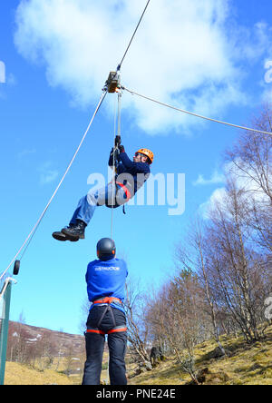 young man reaching the end of the zipwire and being aided down by the instructor Stock Photo