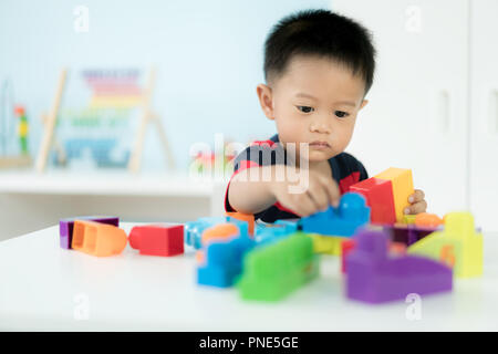 Adorable Asian Toddler baby boy sitting on chair and playing with color block toys at home. Stock Photo
