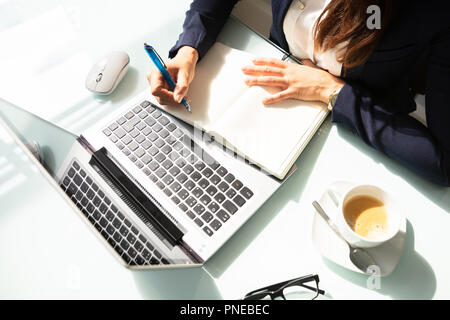 Close-up Of A Businesswoman's Hand Writing Note With Pen In Diary Over Desk Stock Photo