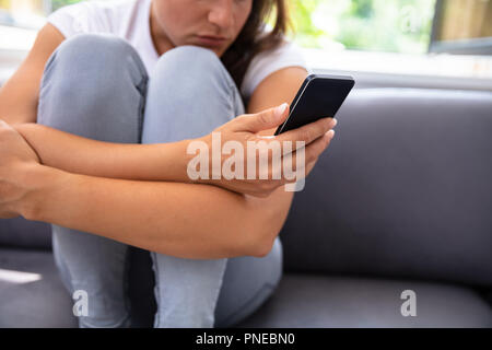 Young Woman Sitting On Sofa Using Smartphone Stock Photo
