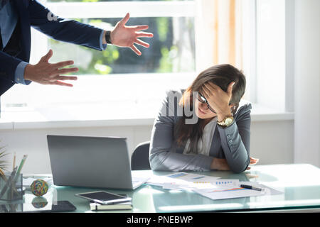 Businessman Scolding Stressed Female Employee Sitting In Office Stock Photo