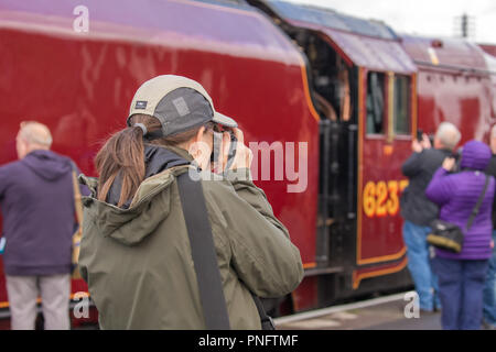 Kidderminster, UK. 21st September, 2018. Day Two of Severn Valley Railway's Autumn Steam Gala sees excited trainspotters flocking to the platform at Kidderminster SVR vintage station. Despite the rain showers, train enthusiasts take every opportunity to get as close as they can to these magnificent UK steam locomotives, particularly the Duchess of Sutherland looking resplendent in her fine crimson livery. A female photographer (rear view) is seen taking photographs of the busy platform scene at this heritage railway. Credit: Lee Hudson/Alamy Live News Stock Photo