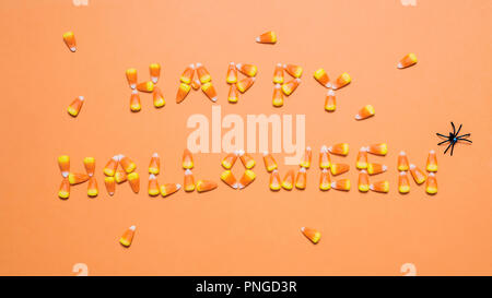 Candy corn spelling out the words Happy Halloween with plastic spiders on an orange background Stock Photo