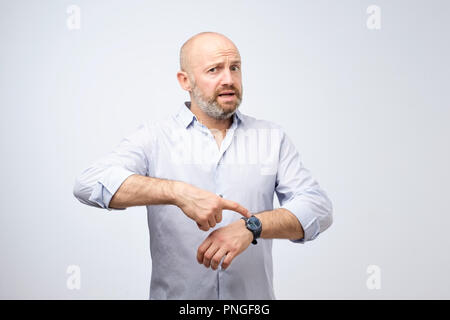 Mature european businessman impatiently pointing to his watch. Why are you late concept. I am waiting here for hours. Stock Photo