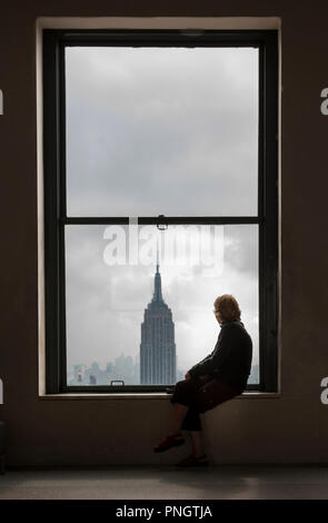 New York, USA. 05th October, 2008. A woman sits on a window ledge looking at the view of the Empire State Building and Manhattan in New York, USA Stock Photo