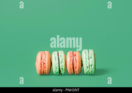 Mint green and orange macarons lined up on their side on a green background with space for copy and text Stock Photo