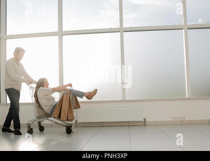 view from afar.a man carries his girlfriend in a shopping cart Stock Photo