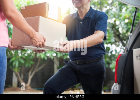 Woman receiving parcel cardboard box from delivery man Carrying Courier Shipping Mail from making an online order while standing in front of the house Stock Photo