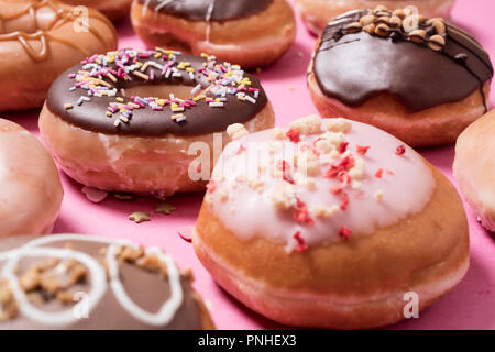 Assorted donuts on a pink background.  Includes classic chocolate sprinkles donut as well as strawberries and cream with scattered sprinkles and heart Stock Photo