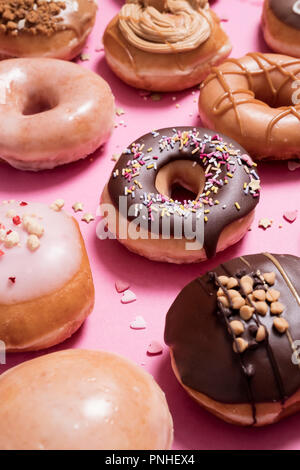 Assorted donuts on a pink background.  Includes classic chocolate sprinkles donut as well as strawberries and cream with scattered sprinkles and heart Stock Photo