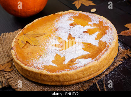 American homemade pumpkin pie with cinnamon and nutmeg, pumpkin seeds and autumn leaves on a wooden table. Thanksgiving food. Stock Photo