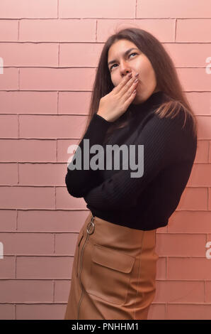 Close-up vertical portrait of a beautiful girl in a black jacket and a brown skirt that misses. The model is of crimson brick background Stock Photo