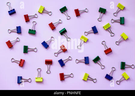 Metal binder colorful clips on violet background, office and school stationery, top view, texture. Place for text, concept of workplace, back to schoo Stock Photo