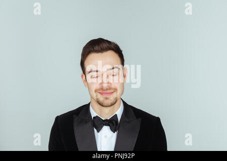 Portrait of a young handsome man in a tuxedo,  smiling and looking at the camera, against pl​ain studio background. Stock Photo