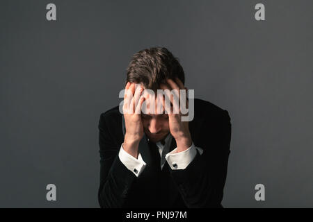 Close up portrait of a young handsome man in a dinner jacket, bow tie undone, looking down, against plain studio background Stock Photo