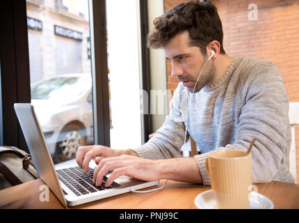 Young man listens to and write on computer with cup of coffee Stock Photo