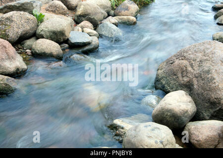 Small creek with stony bottom, rapid stream running between boulders, smoothed water surface