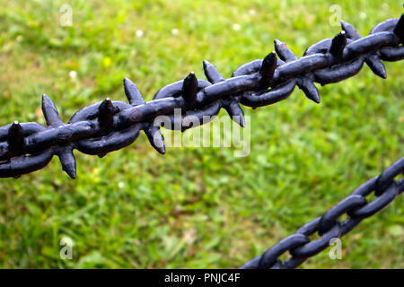 Old black painted massive iron chains with spikes against green grass field Stock Photo