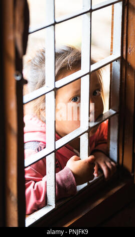 GHALEGAUN, NEPAL - CIRCA MAY 2018: Young Nepali girl looking through an open window with grill. Stock Photo
