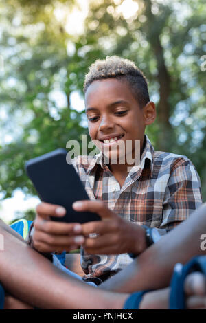 Cute cheerful nice boy looking at his smartphone Stock Photo