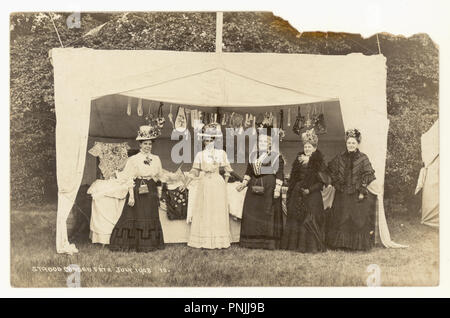 Original Edwardian era summertime photographic postcard of ladies at Strood Garden Fete posing for a photograph by a stall selling hand sewn gifts and handmade crafts - wonderful images of hats, women of different ages, stunning outfits. Postcard dated July 1908, Strood, Kent, U.K. Stock Photo