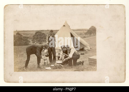 Edwardian postcard of young men camping in the countryside, cooking on an open fireout outside canvas tent, circa 1904, U.K Stock Photo